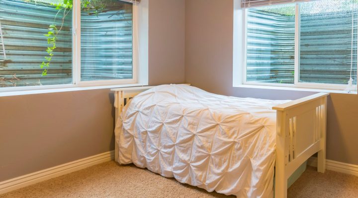 Interior view of a newly installed double-hung egress window in a finished basement bedroom; white frame, sheer blinds, natural light filtering through greenery outside—enhancing safety, ventilation, and aesthetics.