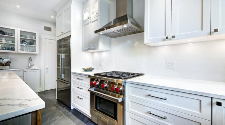 Bright, high-end kitchen with white shaker cabinets, marble island countertop, stainless steel range and hood, subway tile backsplash, glass-front upper cabinets, and dark gray porcelain floor tiles—exemplifying clean, functional design.